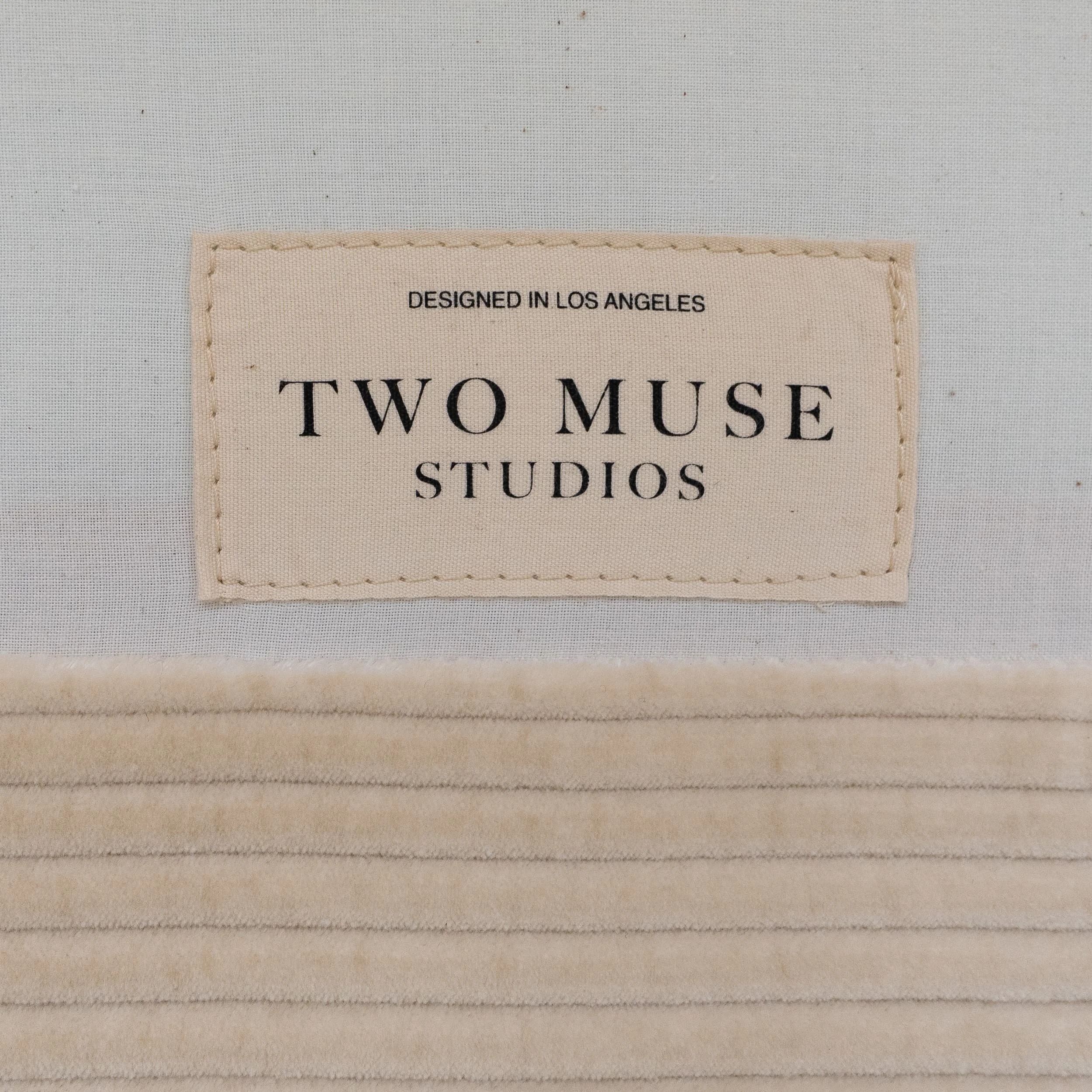 Close-up of a stitched fabric label reading "Two Muse Studios – Designed in Los Angeles" on the underside of an upholstered piece, celebrating the collaboration behind the bespoke office furniture.