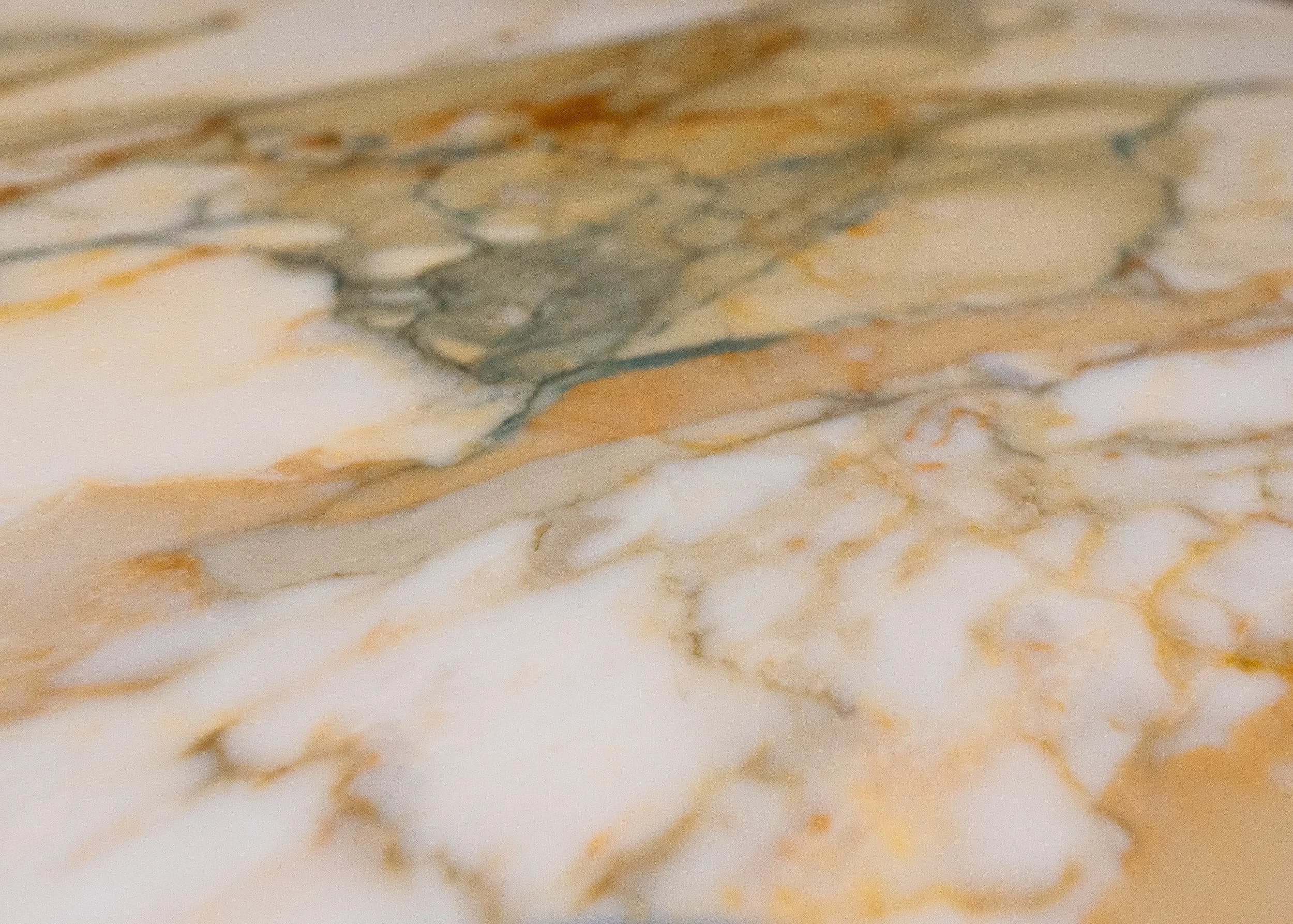 Close-up of richly veined marble surface in warm creams, golds and soft greens used in the bar area, highlighting the elevated material palette that complements the timber furniture and brass details.