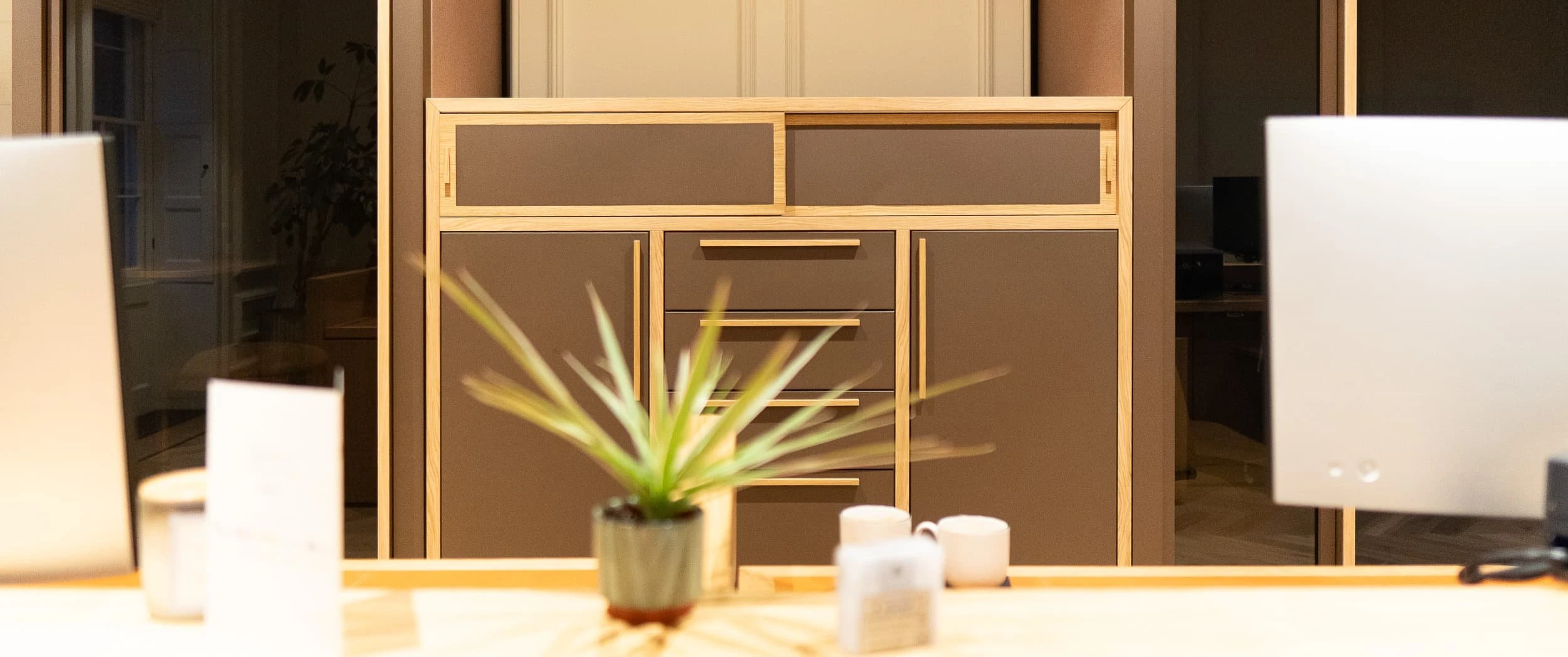 Front view of bespoke oak and taupe lacquer storage behind a desk, with slim framing and recessed panels, acting as refined casegoods that provide generous office storage without visual clutter.