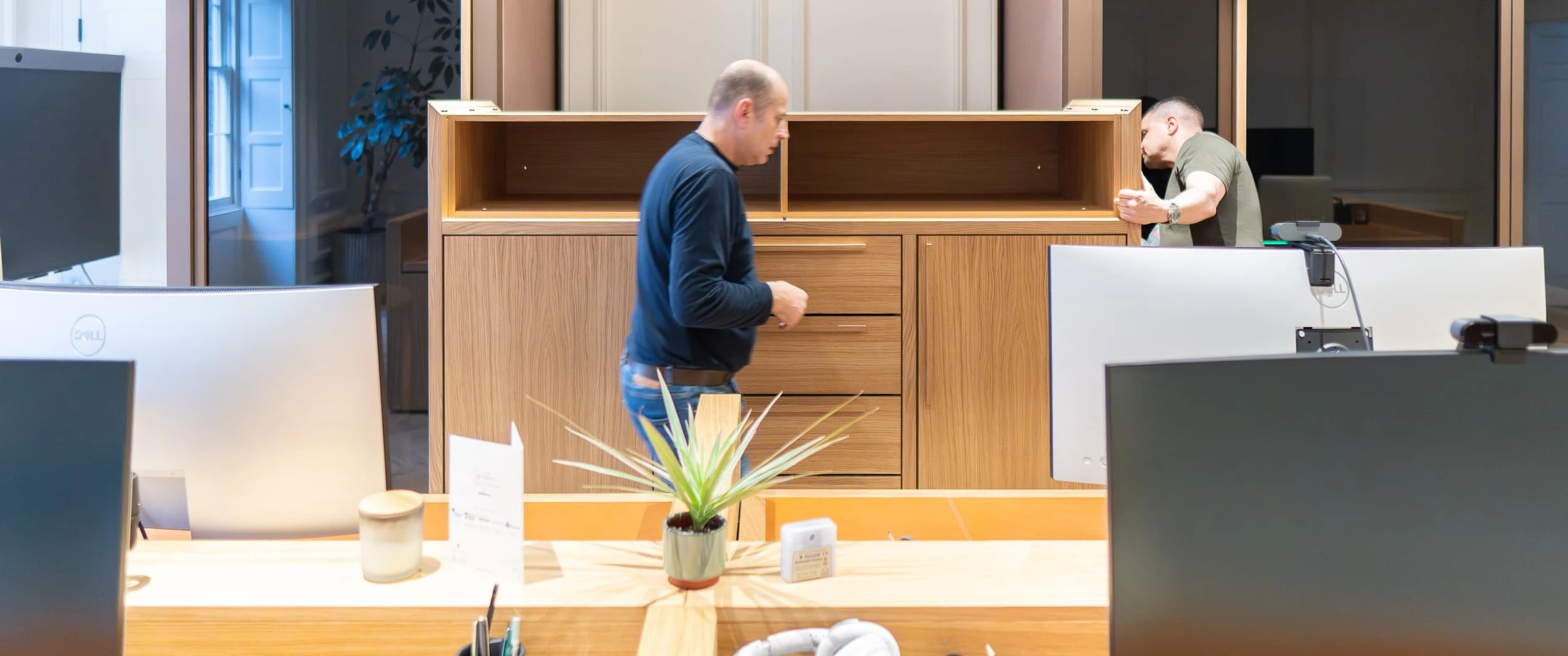 Run of tall oak and lacquer storage integrated into wall panelling, with multiple doors and drawers, providing discreet hidden storage while reading as a considered architectural feature.