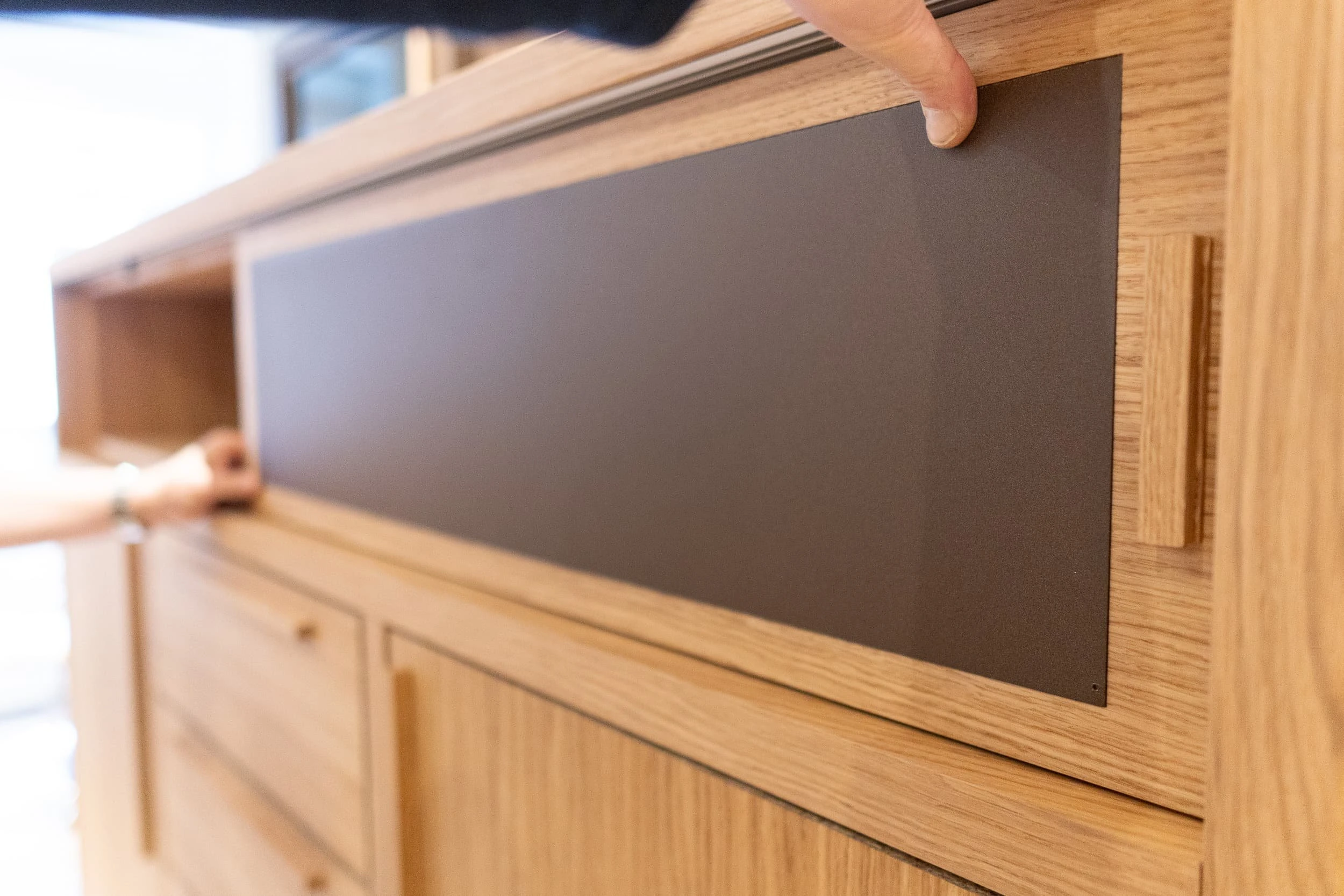 Detail of open oak shelves and closed cupboards within a bespoke credenza, showing precise joints, handleless doors and calm shadow lines that help the storage recede within the office scheme.