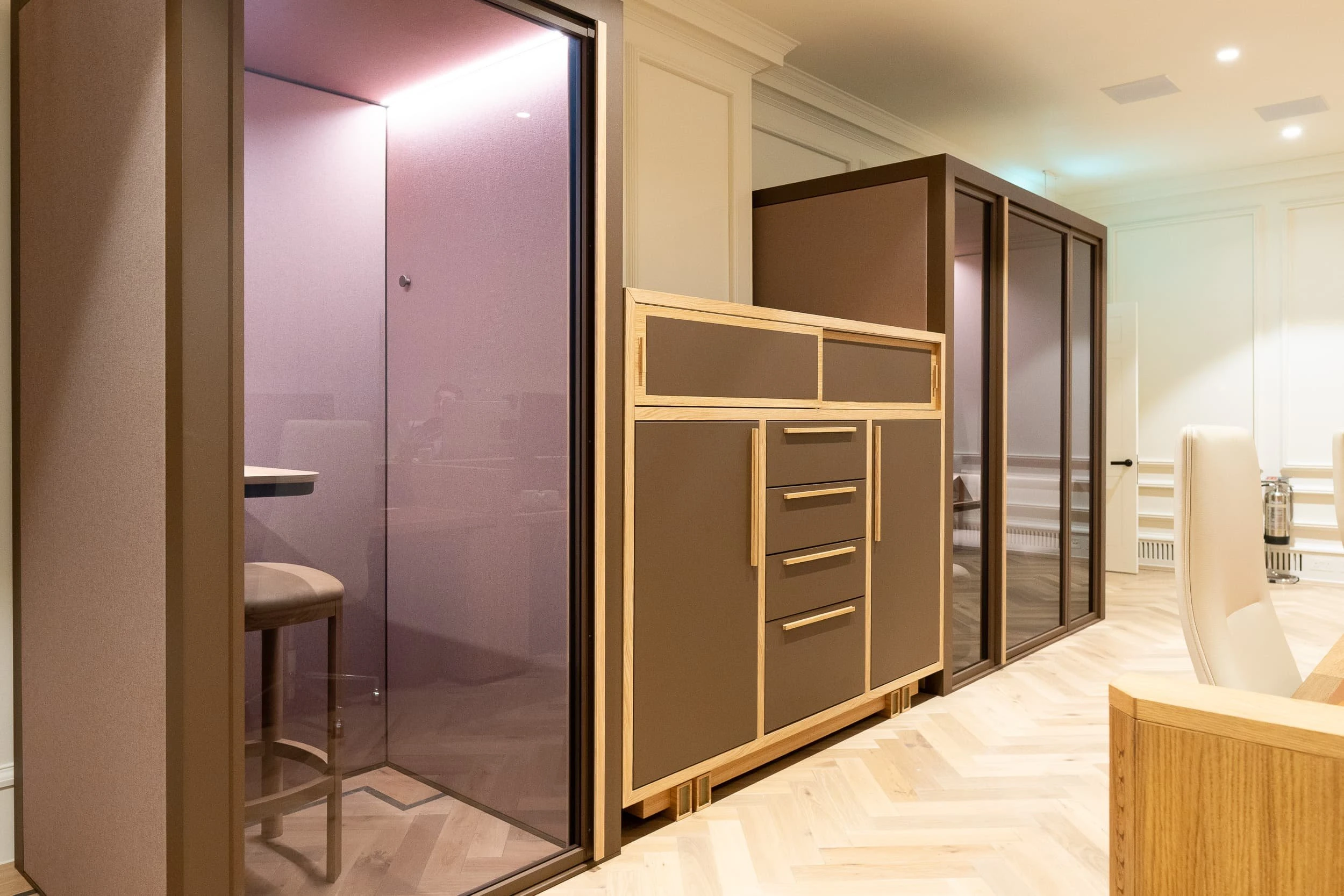Side view along a line of oak-faced storage units sitting on herringbone flooring, demonstrating how the tailored casework acts like built-in furniture in a residential living space.