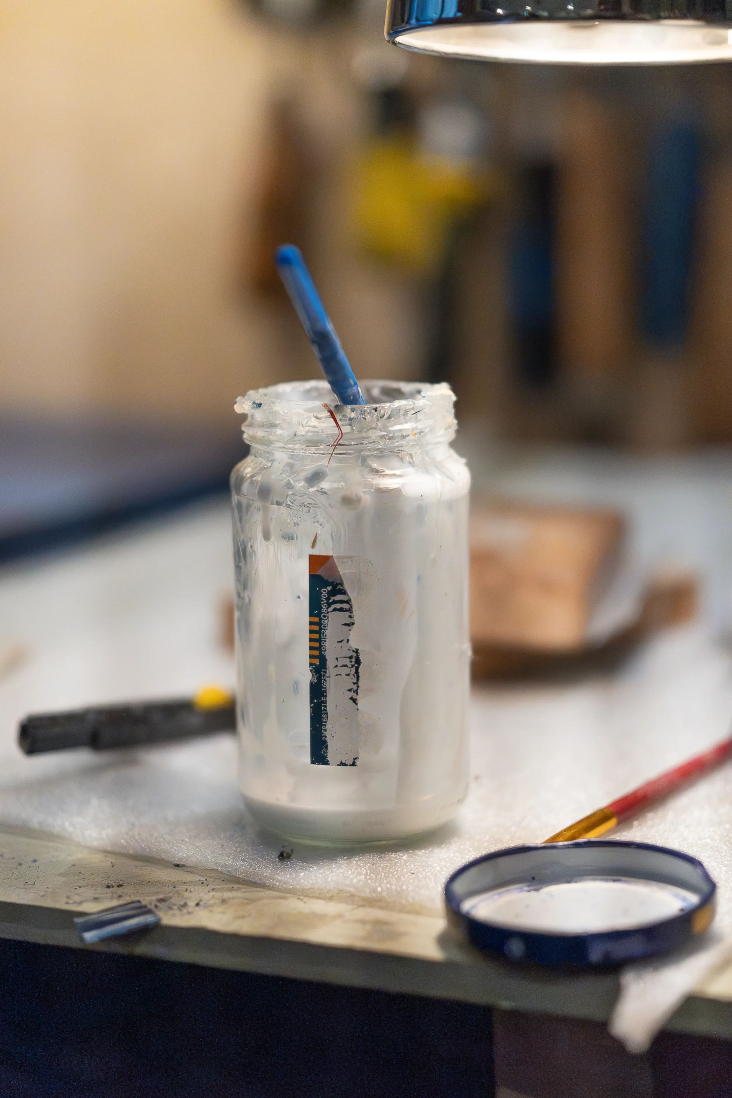 Jar of marquetry adhesive with a brush at the workshop bench, used to lay the dyed straw for the Taman Duta Villa door panels.