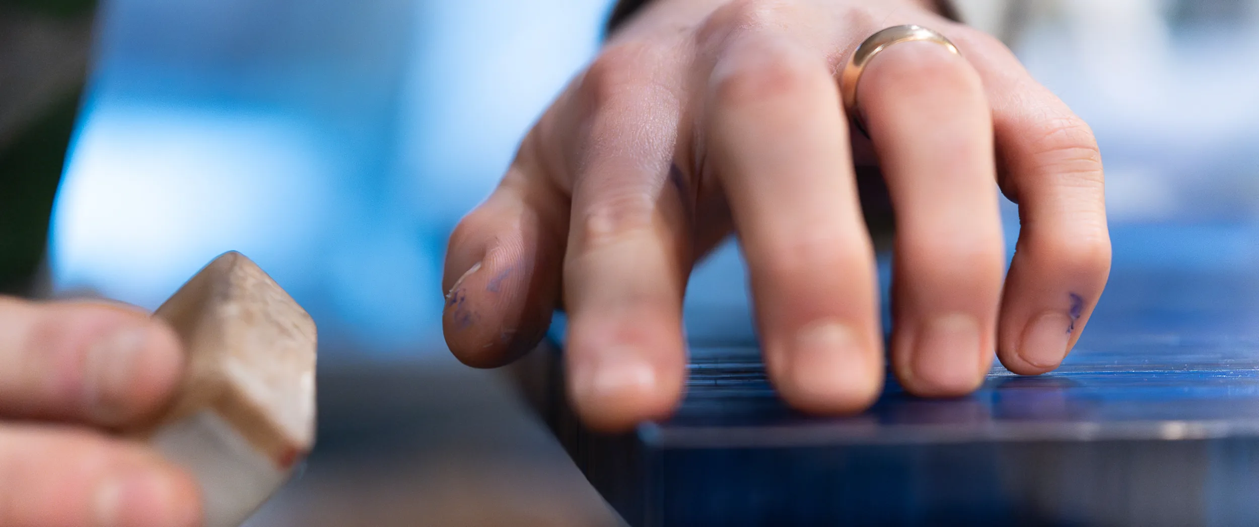 A maker pressing dyed straw down onto a panel by hand, fingertips stained blue from the straw.