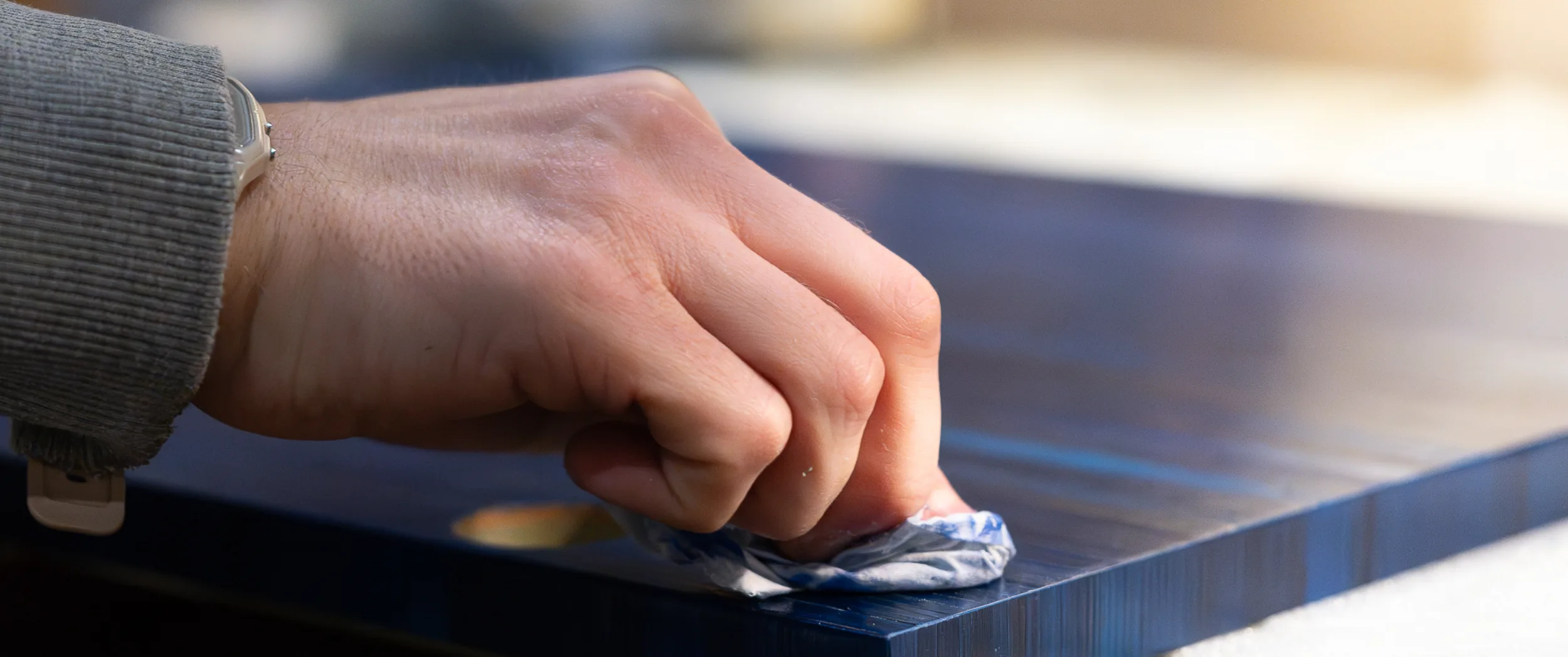 A maker rubbing back the surface of a finished blue straw-marquetry panel with a cloth.