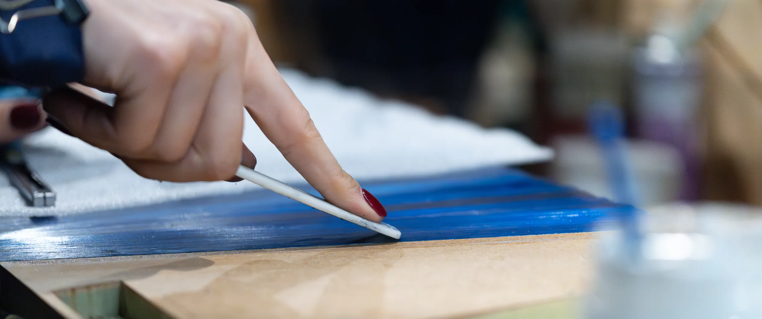 A maker laying a single blue straw with a bone folder, building the marquetry fibre by fibre.