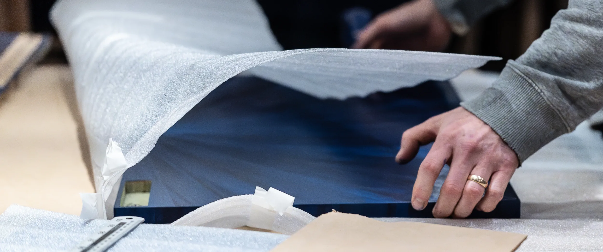 Hands wrapping a finished blue starburst door panel in protective foam, ready for crating and shipping to Kuala Lumpur.