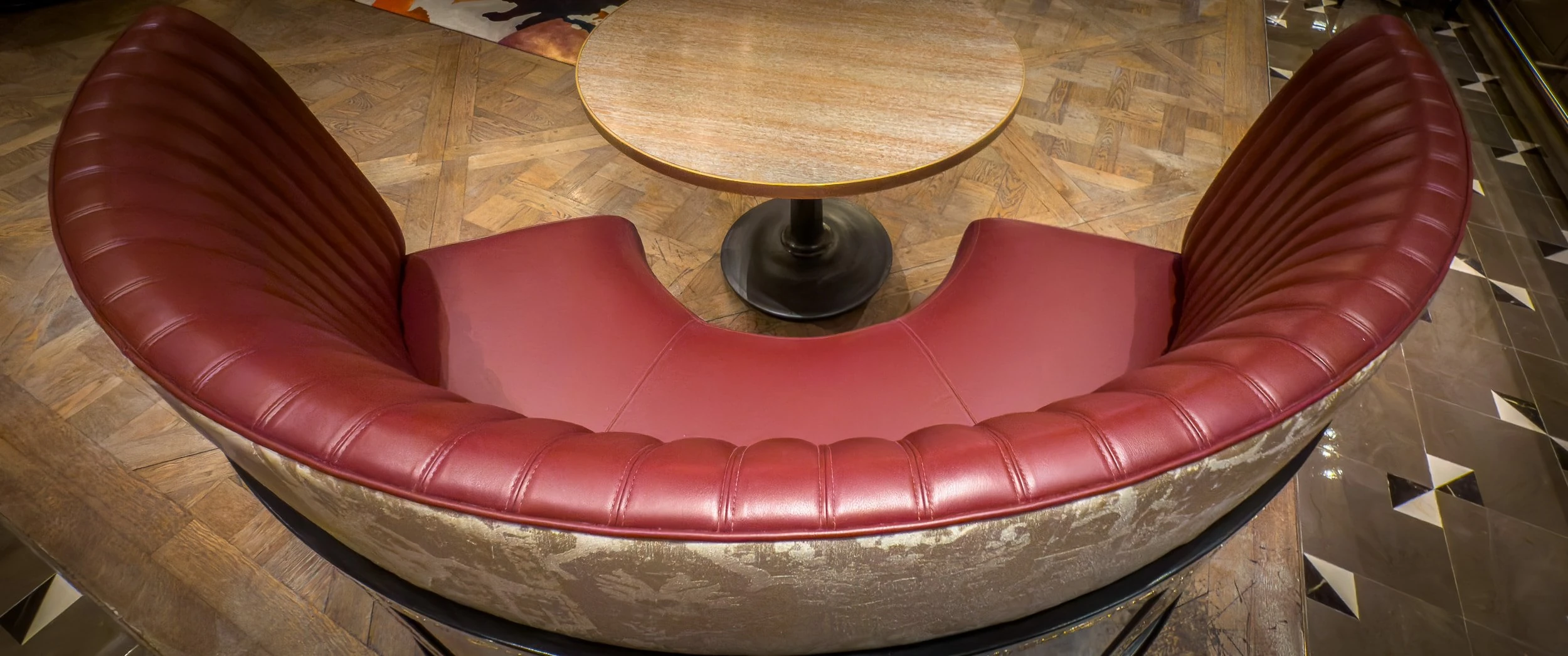 Overhead view of the installed curved banquette at The Grill, with red leather seat and fluted back wrapping a round table on parquet flooring.