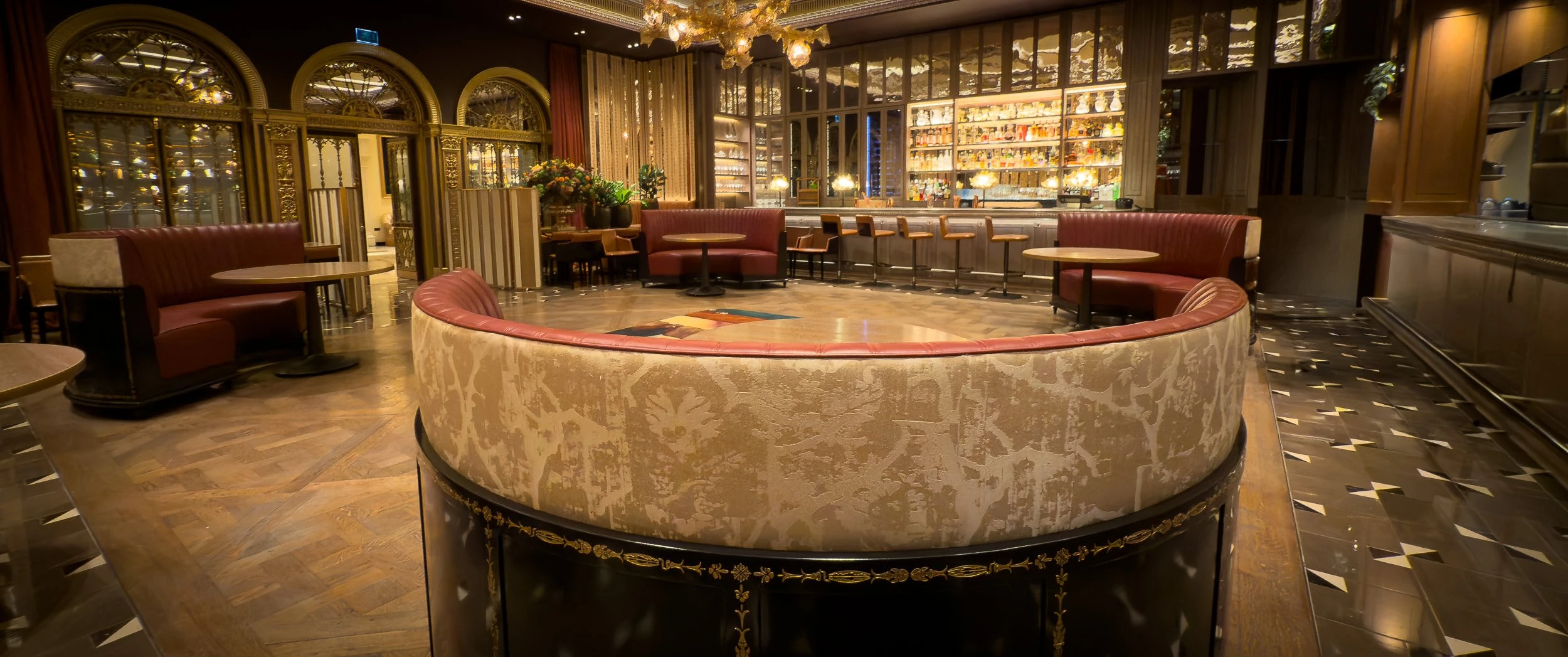 The Grill at The Dorchester at night, with a curved banquette in damask and red leather over a gold-motif lacquered base, set against the bar and further seating beyond.