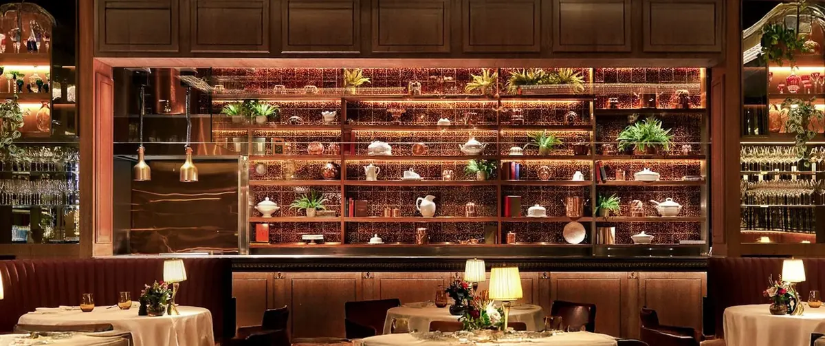 Interior of The Grill at The Dorchester with lit copper shelving above the pass, panelled walls and leather banquettes