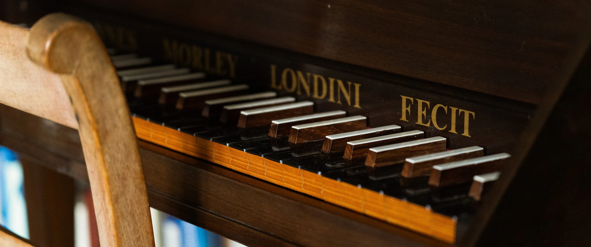 Close detail of a keyboard instrument at Well Cottage, its dark case lettered in gilt with Morley Londini Fecit above stopped wooden keys.